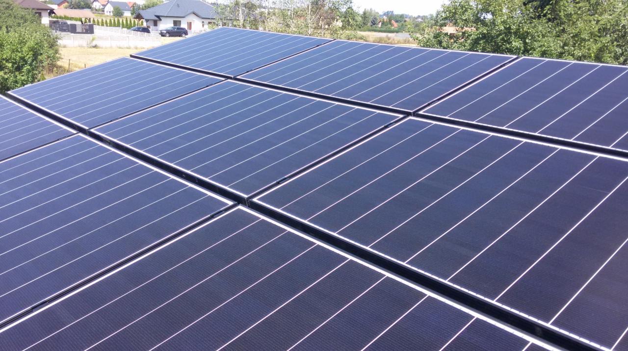 Kompletny system paneli słonecznych na dachu domu jednorodzinnego, widok z góry, w tle zabudowa mieszkalna i zieleń.