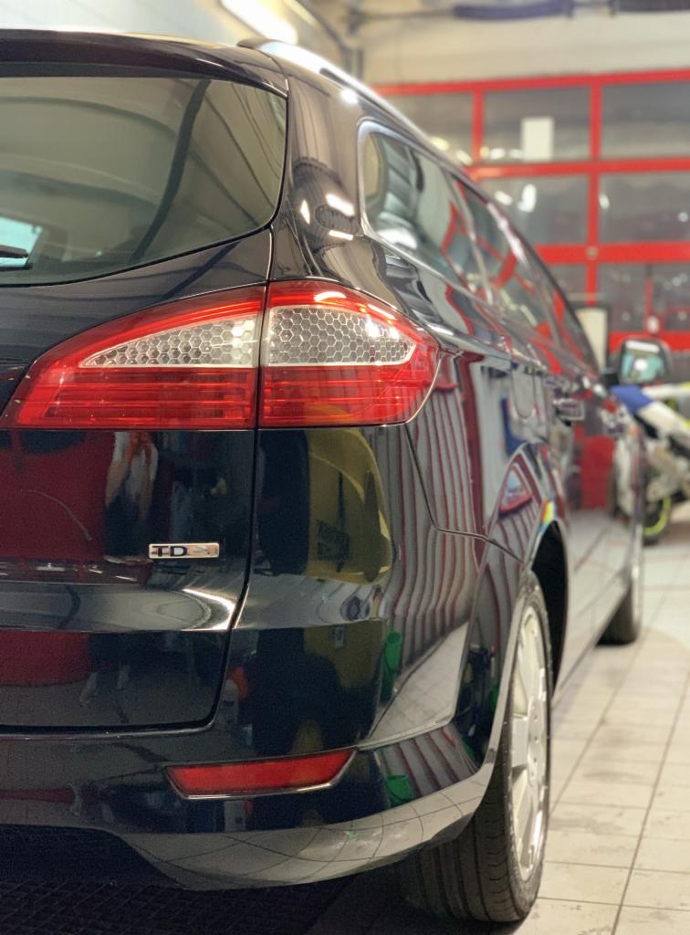 Błyszczący, czarny samochód typu kombi marki Ford, widok z tyłu, po umyciu w myjni; widoczne światła tylne, emblemat TDCI i odbicia w lakierze.