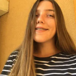 Portret uśmiechniętej nastolatki z aparatem ortodontycznym, stojącej na balkonie z widokiem na budynek.