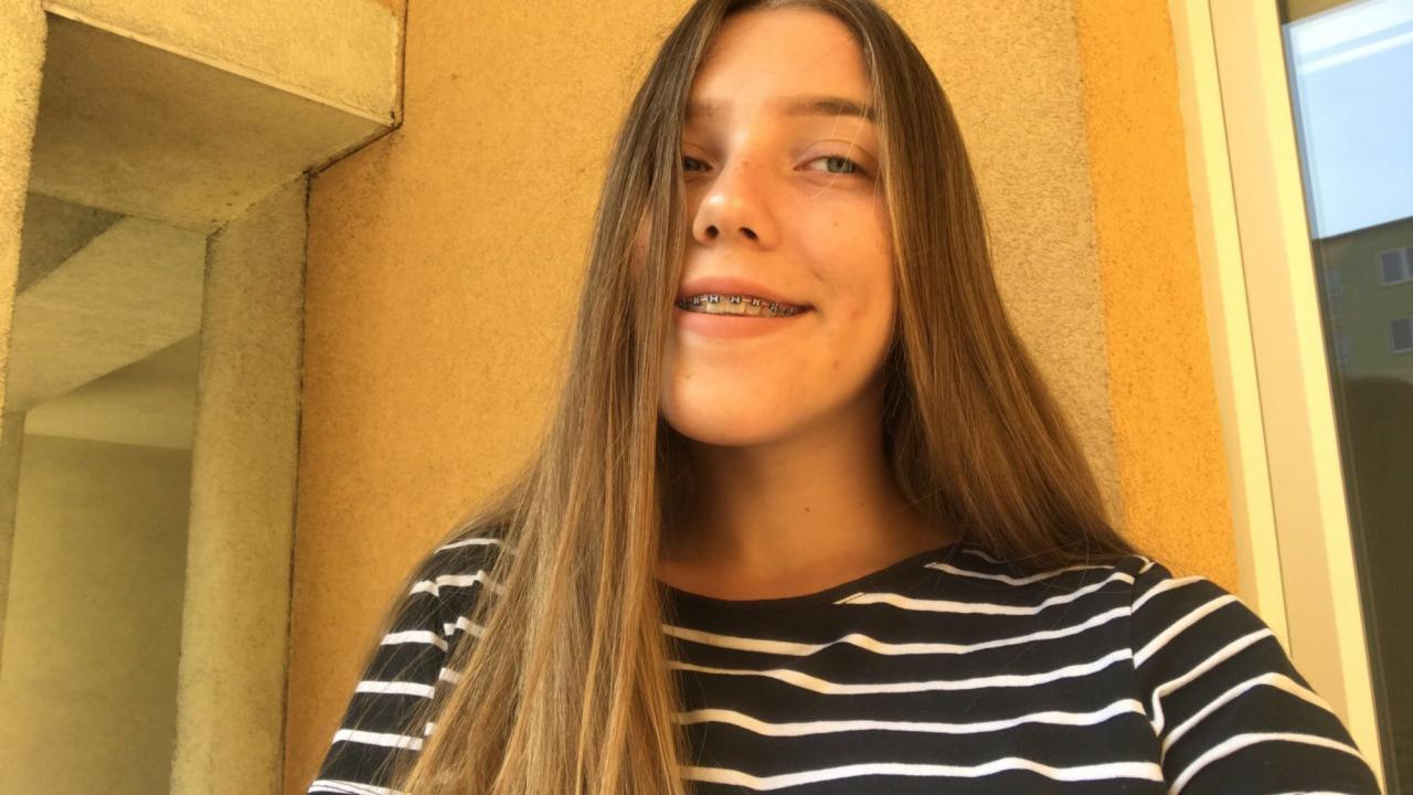 Portret uśmiechniętej nastolatki z aparatem ortodontycznym, stojącej na balkonie z widokiem na budynek.