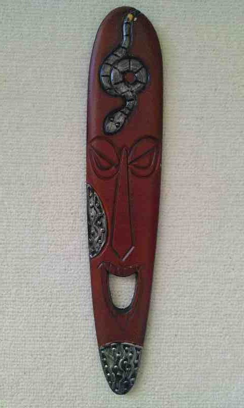 Podłużna, brązowa maska afrykańska z rzeźbioną twarzą, wężem u góry i metalowymi elementami dekoracyjnymi na policzku i dole.