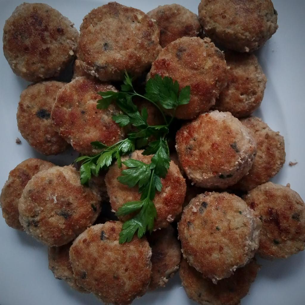 Kompaktowy stos smażonych kotletów mielonych z dodatkiem zieleniny, ułożonych na białym talerzu, widok z góry.