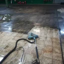 Urządzenie do czyszczenia podłóg przemysłowych w trakcie pracy, widoczny efekt czyszczenia na brudnych płytkach podłogowych w hali.