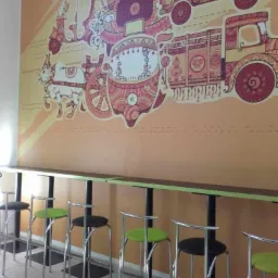 Wysoki blat barowy z krzesłami w lokalu z dekoracyjną ścianą z motywami transportu azjatyckiego.