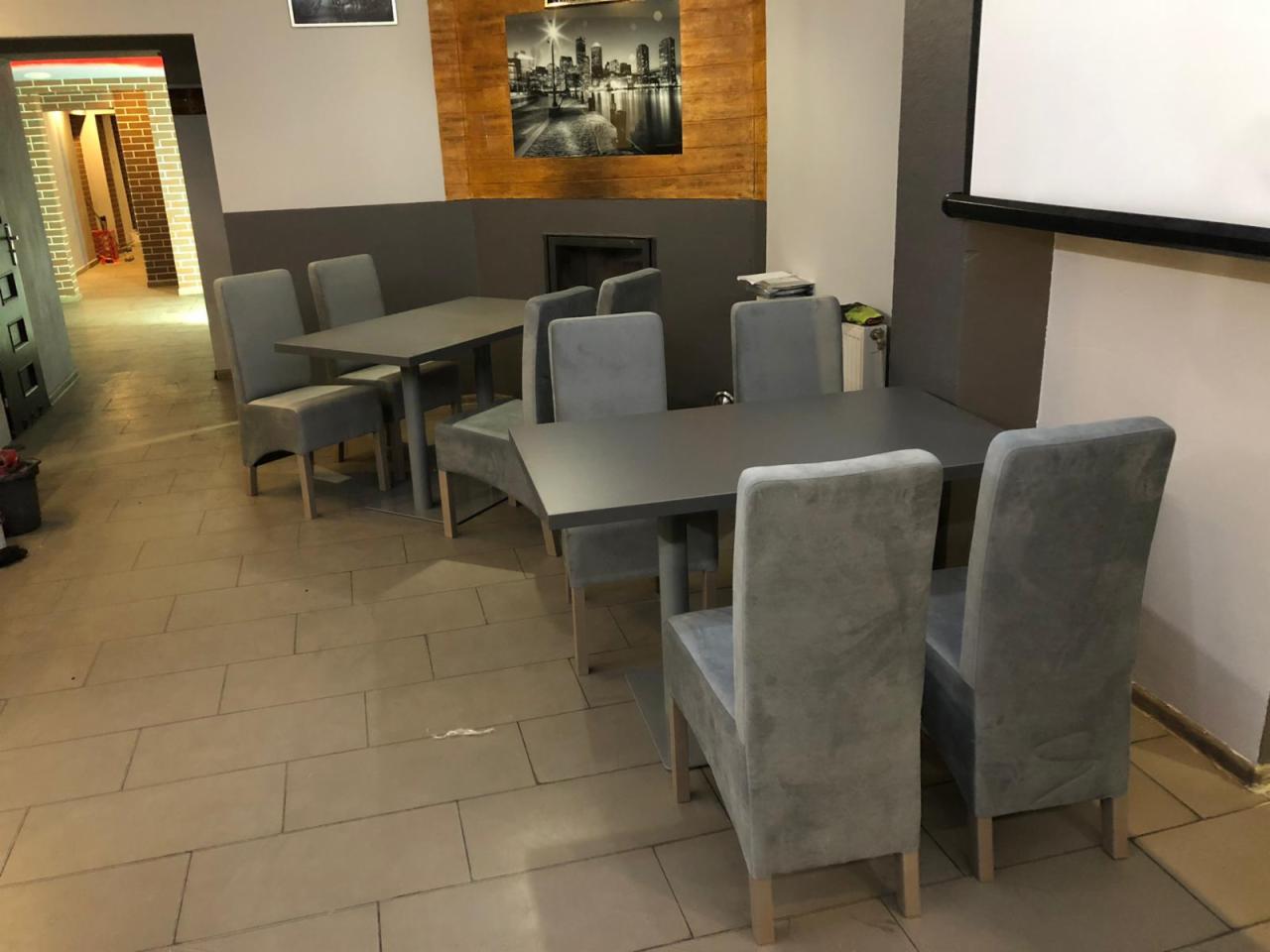 Szare krzesła tapicerowane z wysokim oparciem i ciemne stoły w sali konferencyjnej z rzutnikiem i obrazem miasta na ścianie.