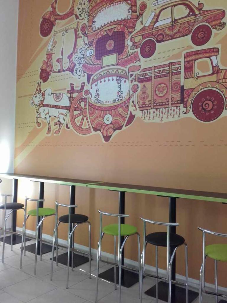 Wysoki blat barowy z krzesłami w lokalu z dekoracyjną ścianą z motywami transportu azjatyckiego.