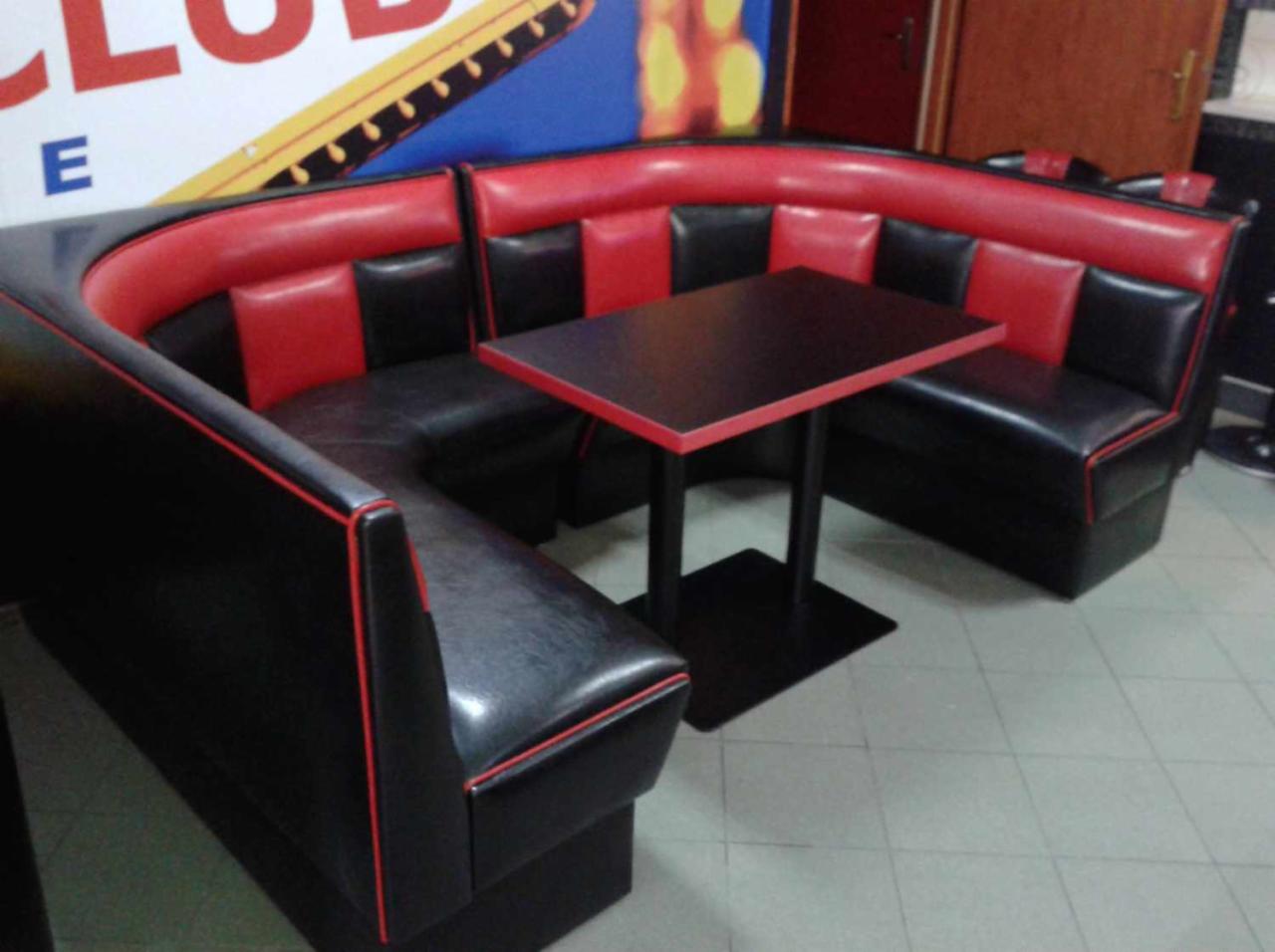 U-kształtna, czarno-czerwona loża z tapicerowanymi siedzeniami i oparciami, uzupełniona czarnym stołem z czerwonym obramowaniem, w lokalu gastronomicznym.