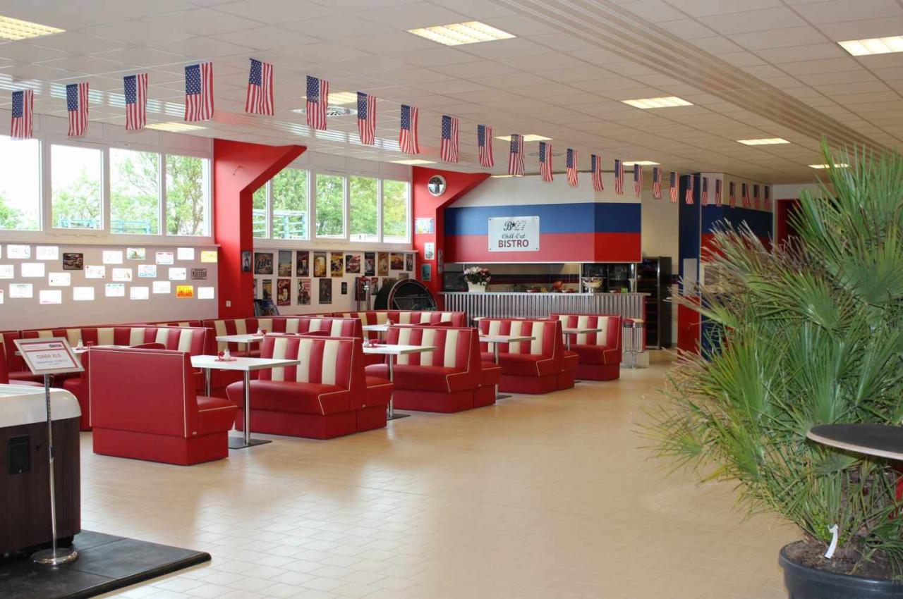 Wnętrze baru w stylu amerykańskim z czerwonymi kanapami w białe pasy, stolikami i dekoracjami w postaci flag USA.