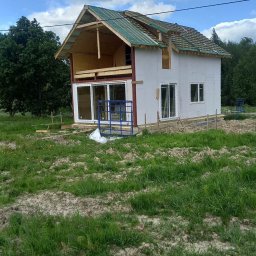 EZ CORP. SPÓŁKA Z OGRANICZONĄ ODPOWIEDZIALNOŚCIĄ - Budowa domu szkieletowego w toku: widoczne ściany z płyt OSB, częściowo pokryty dach z zieloną membraną, okna PCV i rusztowanie na trawiastym terenie.