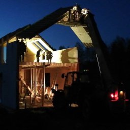 EZ CORP. SPÓŁKA Z OGRANICZONĄ ODPOWIEDZIALNOŚCIĄ - Budowa domu szkieletowego w nocy: ekipa montuje elementy konstrukcyjne przy użyciu dźwigu teleskopowego. Widoczna konstrukcja, drewniane elementy i sylwetki robotników.