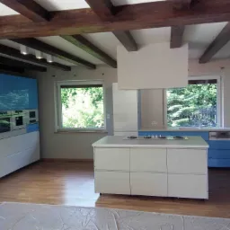 Nowoczesna kuchnia z drewnianymi belkami stropowymi, jasnymi meblami i niebieskimi akcentami, częściowo zabezpieczona folią malarską.