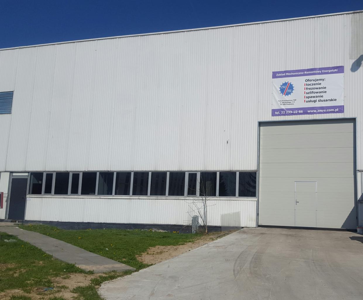 Budynek Zakładu Mechaniczno-Remontowego Energetyki z ofertą usług: toczenie, frezowanie, szlifowanie, spawanie i usługi ślusarskie, widoczny plakat reklamowy z numerem telefonu i adresem strony...