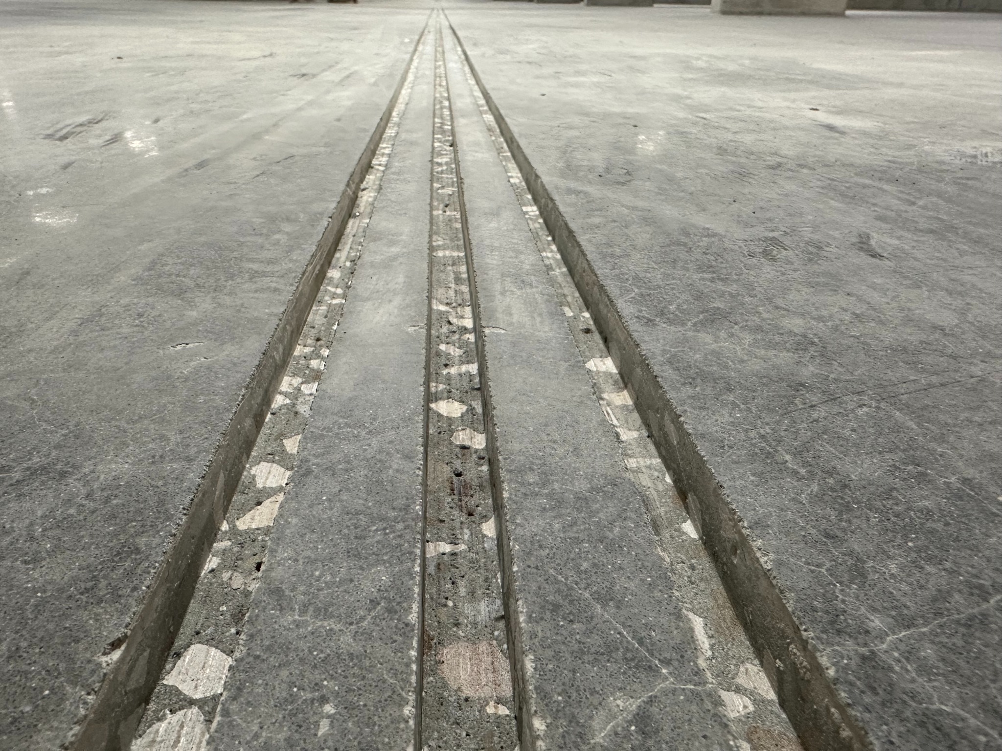 Szlifowana, betonowa posadzka z widocznymi dylatacjami. Szara, surowa powierzchnia z fakturą kamienia. Widok z perspektywy podłogi.