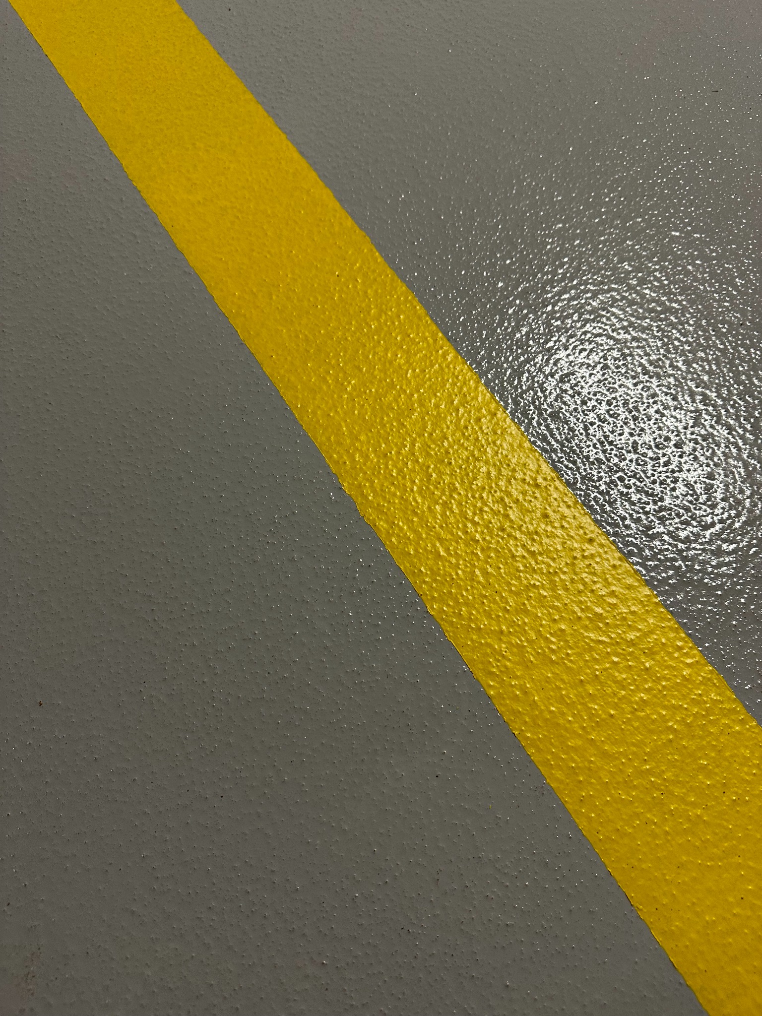 Szara posadzka z żywicy epoksydowej z żółtym, ukośnym pasem ostrzegawczym. Realizacja z Krakowa.