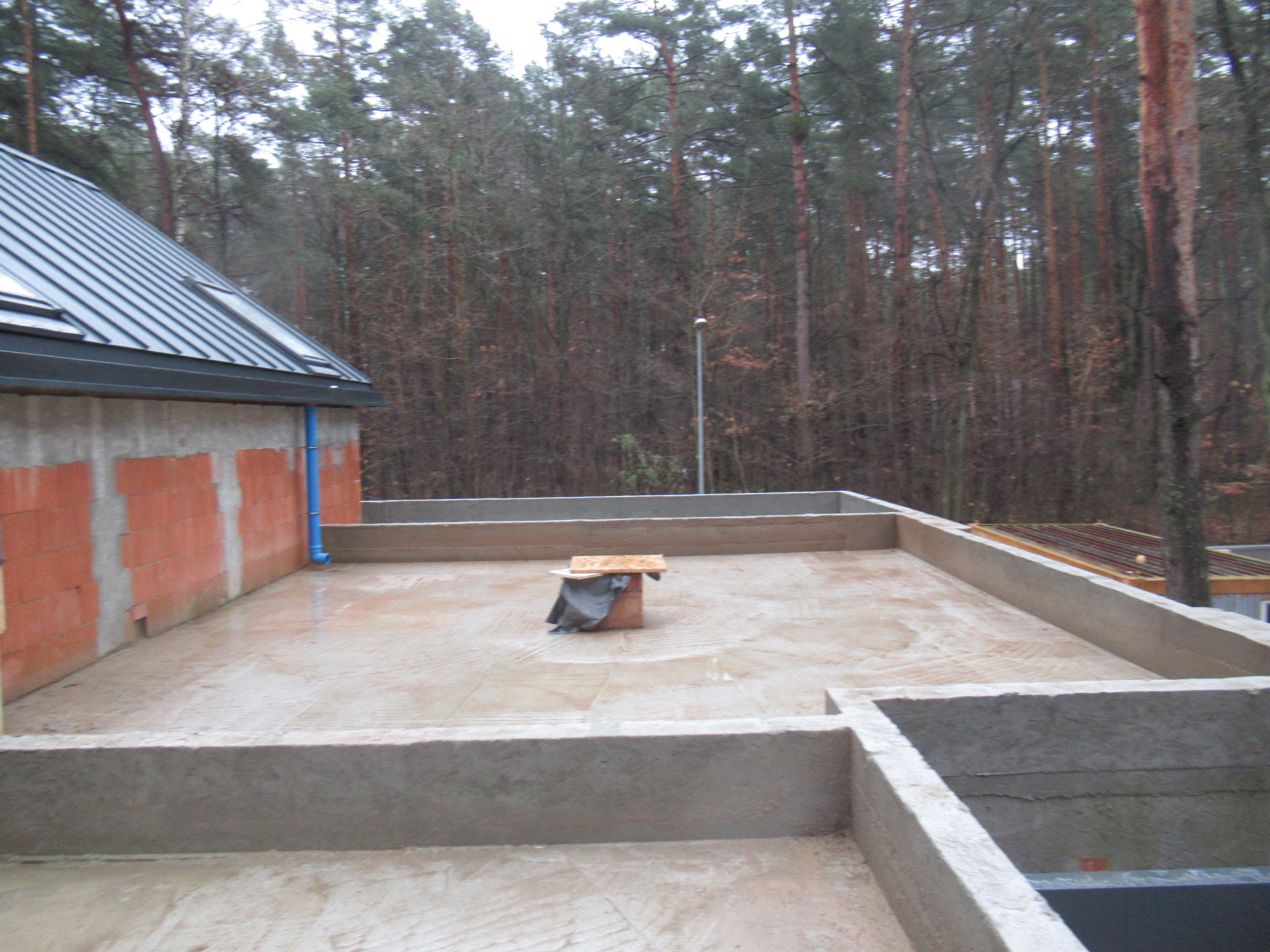 Surowy stan wylewki stropu na budowie domu jednorodzinnego, widoczne bloczki Ytong na ścianach, w tle las.