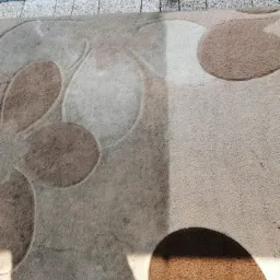 Fragment dywanu z okrągłym wzorem, widoczny obszar po czyszczeniu, kontrastujący z zabrudzoną częścią, oświetlony cieniem słupka.