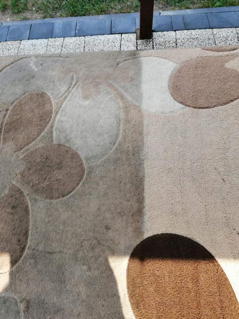 Fragment dywanu z okrągłym wzorem, widoczny obszar po czyszczeniu, kontrastujący z zabrudzoną częścią, oświetlony cieniem słupka.