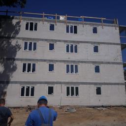 ArkadiaSp. z o.o. - Wznoszony, trzypiętrowy budynek z betonu komórkowego z zamontowanymi oknami, widoczne szalunki stropowe na dachu, teren budowy z dwoma robotnikami w tle.