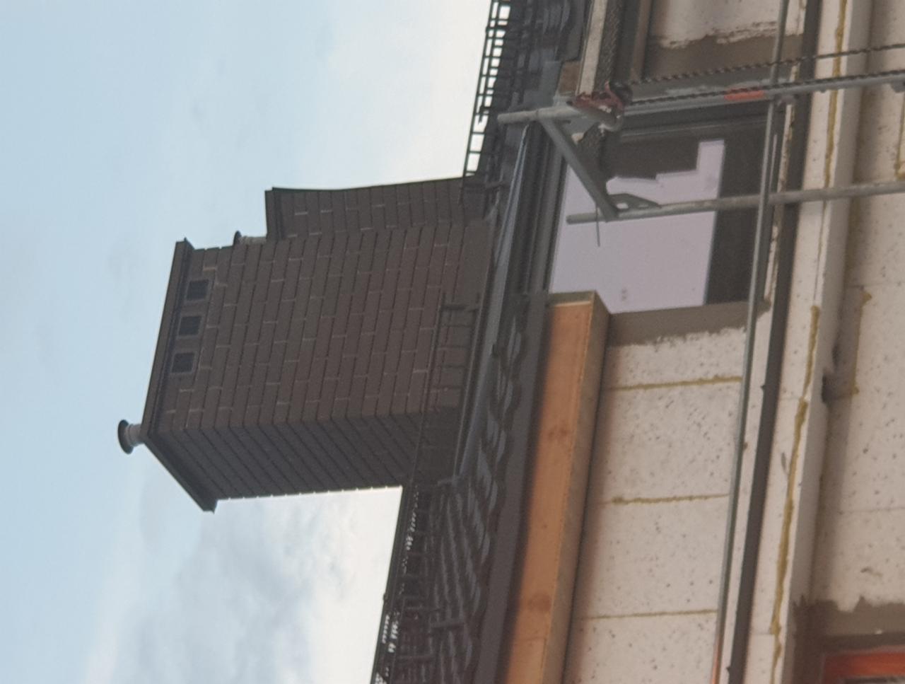 Wznoszony komin z cegły na budynku w trakcie budowy, widoczne rusztowanie i okno.