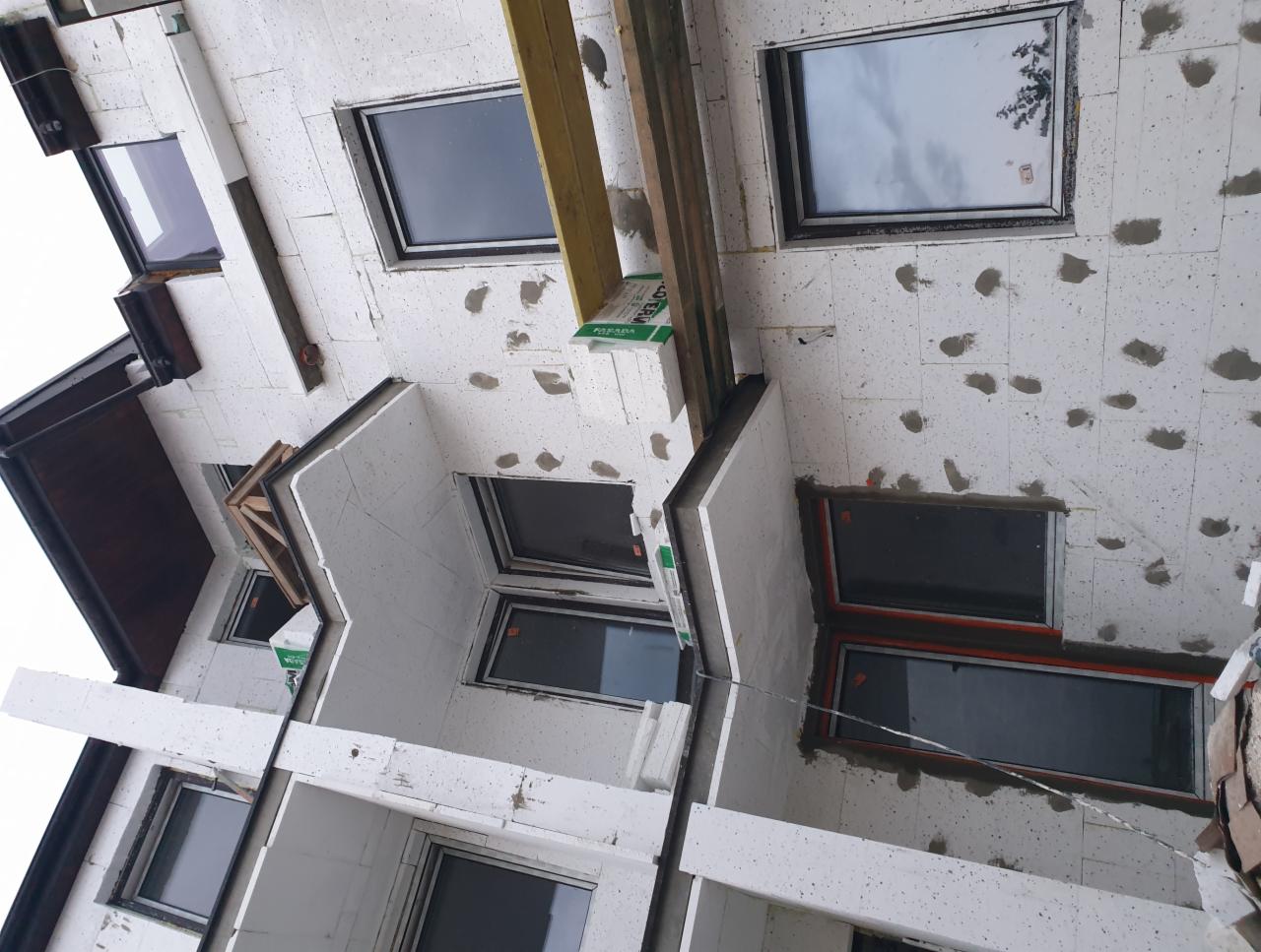 Surowy stan budynku w trakcie budowy, widoczne okna, białe ściany z betonu komórkowego i drewniane elementy konstrukcyjne.