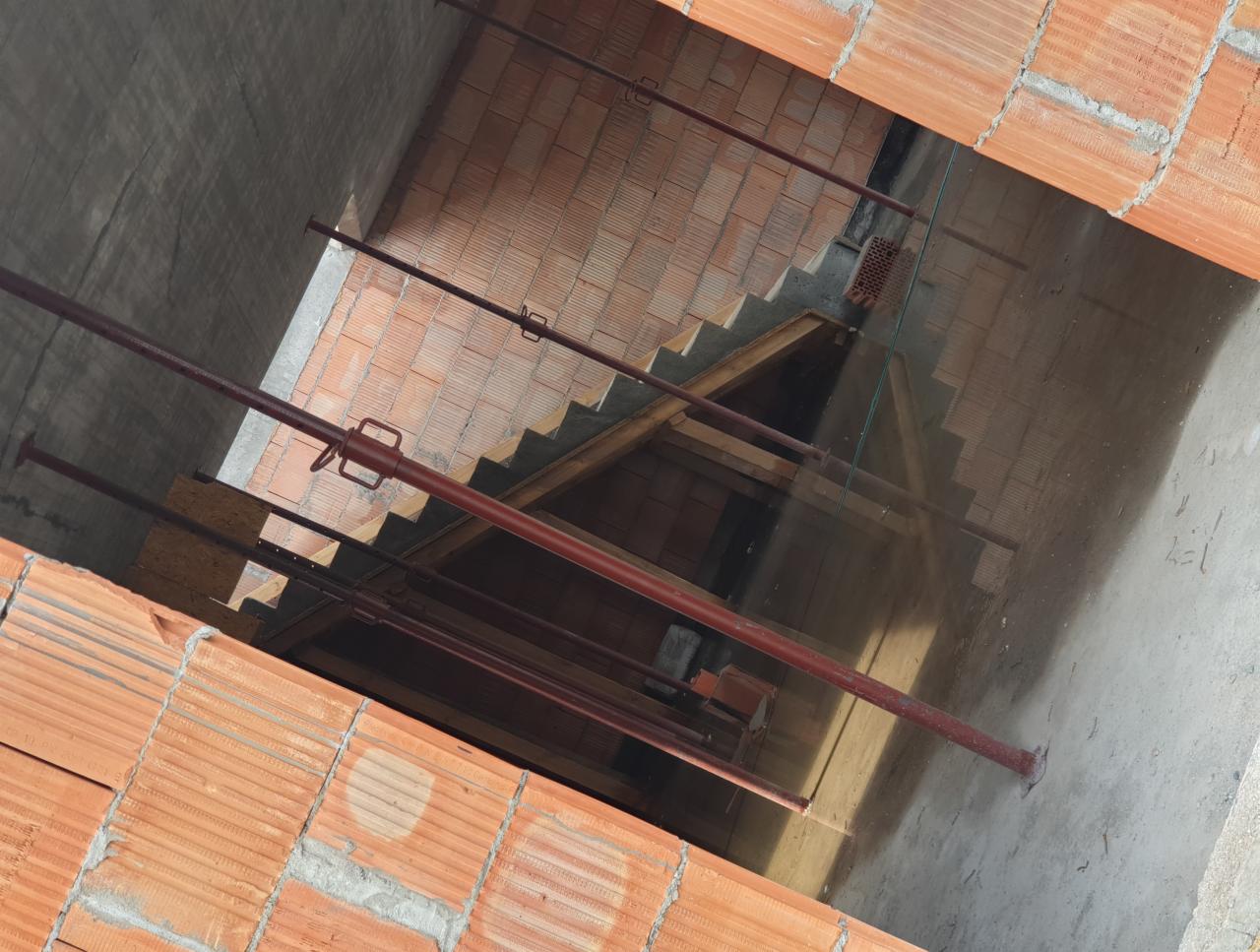 Wnętrze budowanego domu z czerwonej cegły, widoczne podpory stropu i schody w surowym stanie.