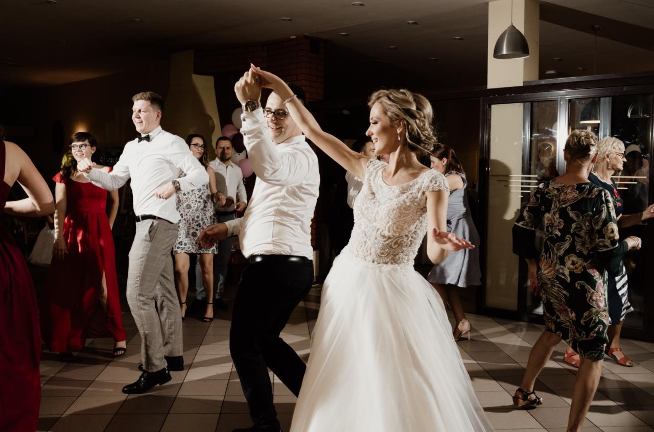 Para młoda tańczy na parkiecie podczas wesela, w tle goście i dekoracje.