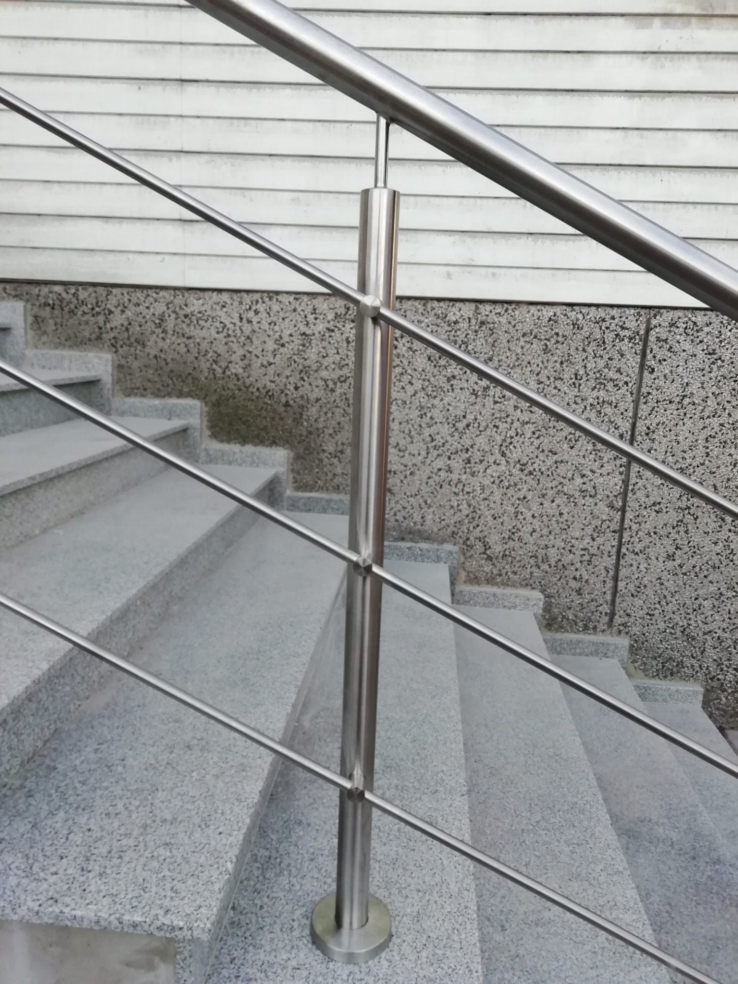 Szare granitowe schody z balustradą ze stali nierdzewnej z wypełnieniem linkami, widok z dołu, minimalistyczny design.