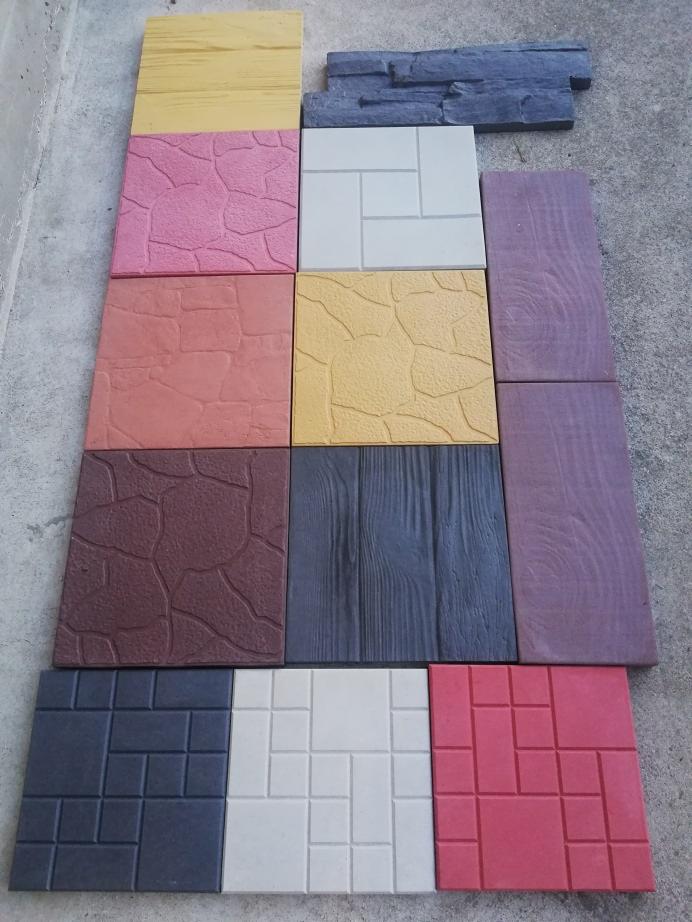 Różnokolorowe płyty chodnikowe o różnych fakturach ułożone na betonowej powierzchni, prezentacja wzorów i kolorystyki.