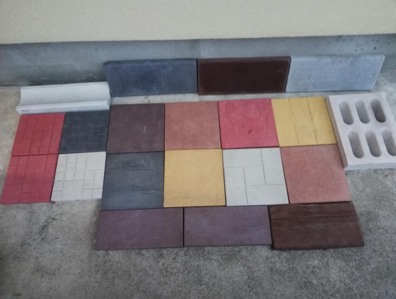Różnokolorowe próbki kostki brukowej i płyt chodnikowych o różnych fakturach i kształtach, ułożone na szarym tle.