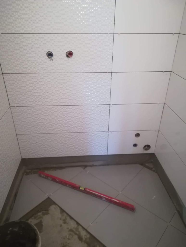 Świeżo ułożone białe płytki na ścianach i podłodze w trakcie remontu łazienki, widoczny poziomica i otwory pod instalacje.