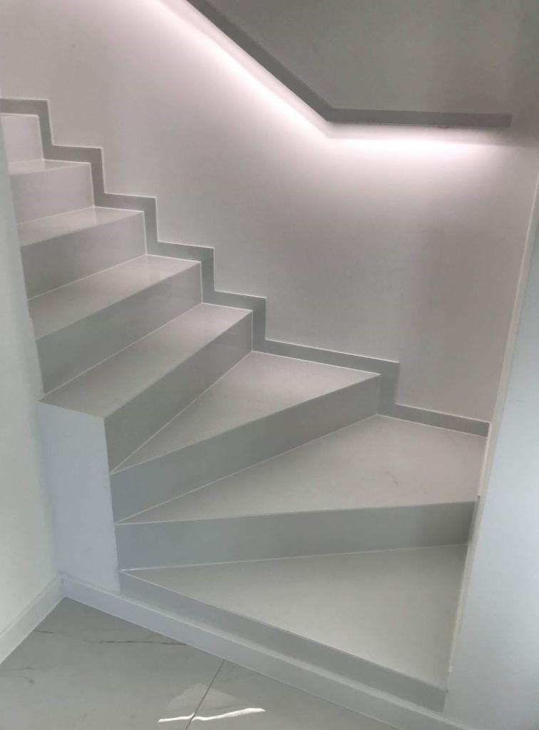Nowoczesne, minimalistyczne schody wykończone szarą glazurą, z subtelnym oświetleniem LED wzdłuż sufitu i marmurową posadzką na dole.