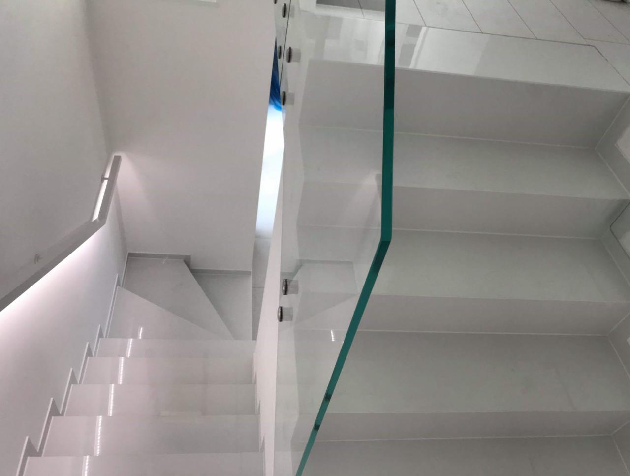 Białe marmurowe schody z szklaną balustradą, widok z góry, oświetlenie LED wzdłuż ściany.