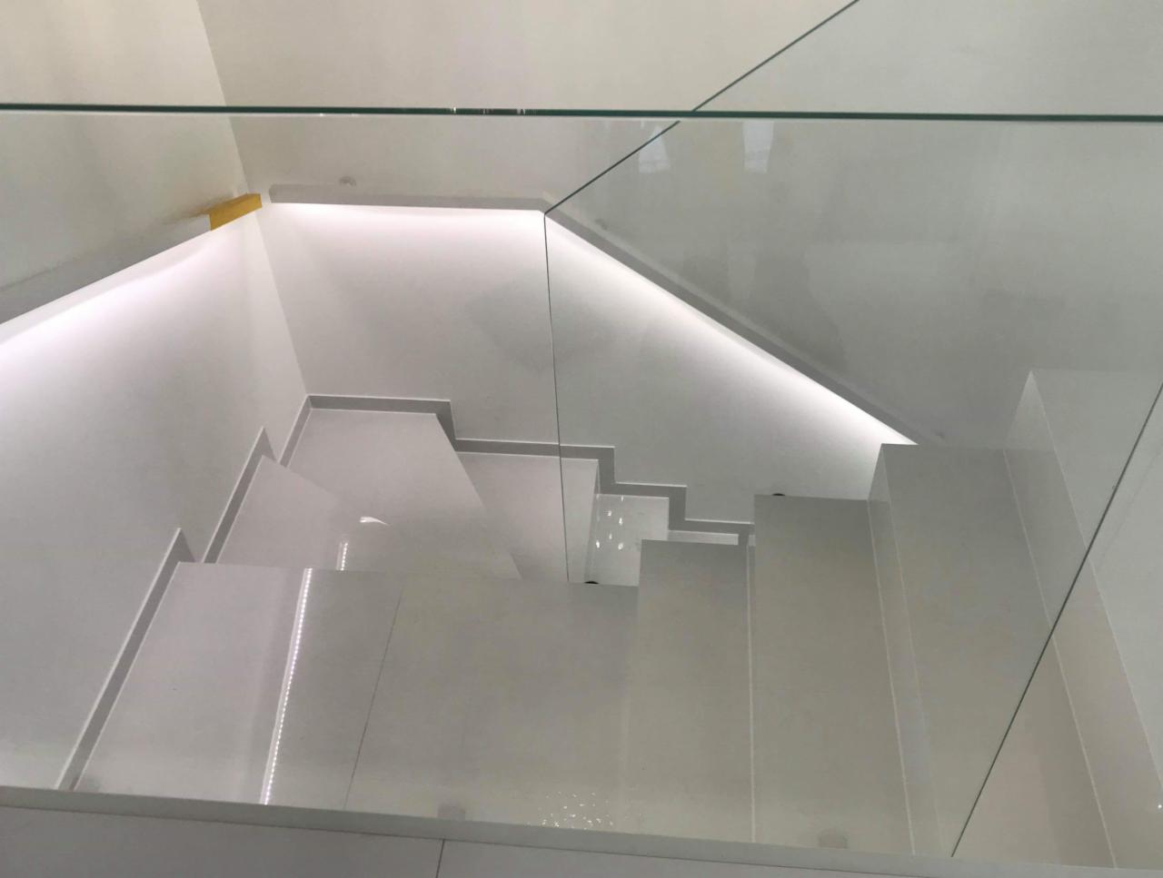 Nowoczesne, białe schody z podświetleniem LED i szklaną balustradą, widok z góry.