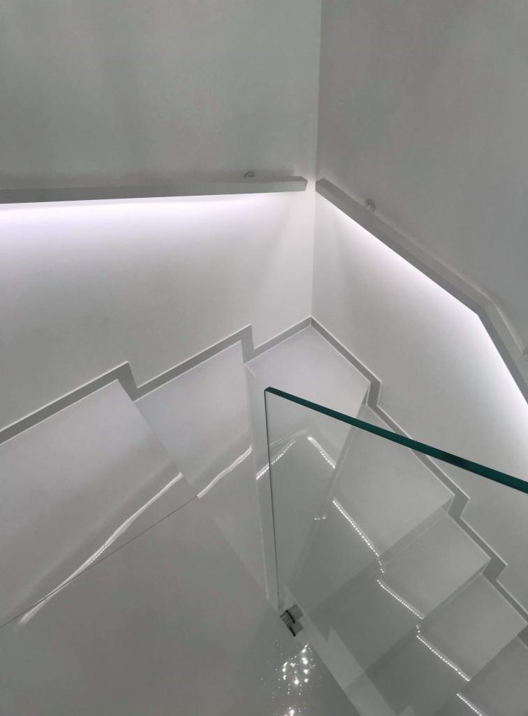 Nowoczesne, białe schody z podświetleniem LED i szklaną balustradą, widok z góry.