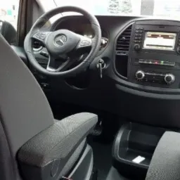 Wnętrze samochodu dostawczego Mercedes Vito, widok z tylnego siedzenia na deskę rozdzielczą i kierownicę z logo Mercedes-Benz.