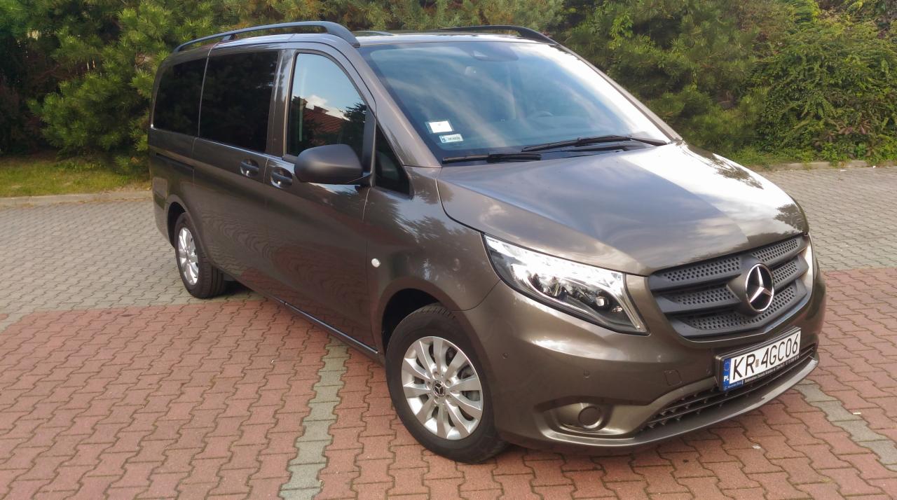 Brązowy Mercedes Vito z relingami dachowymi, zaparkowany na kostce brukowej, z widoczną tablicą rejestracyjną KR 4GC06 i odblaskiem na masce.