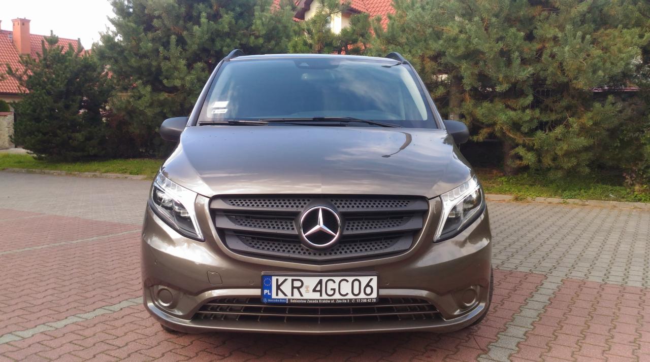 Przód brązowego samochodu Mercedes Vito z polską tablicą rejestracyjną KR 4GC06, zaparkowanego na kostce brukowej przed zielonymi krzewami i domem z czerwoną dachówką.
