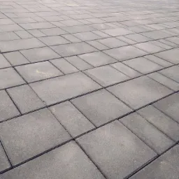 Nowo ułożona, szara kostka brukowa na posesji, widok z niskiej perspektywy, z widocznymi kamieniami i zielenią w tle.