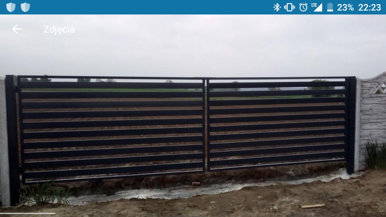 Nowoczesna, metalowa brama przesuwna z poziomymi profilami, zamontowana przy betonowym słupku ogrodzeniowym z dekoracyjnym elementem, widok z zewnątrz posesji.