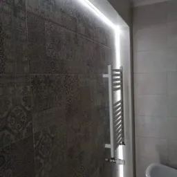 Łazienka z mozaikową ścianą, podświetleniem LED i grzejnikiem drabinkowym.