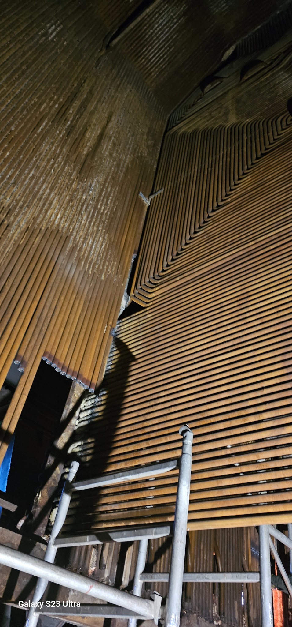 Wnętrze kotła z rzędami rur, widoczne rusztowanie. Specyficzne ułożenie rur i ich stan wskazują na zaawansowany etap prac naprawczych.