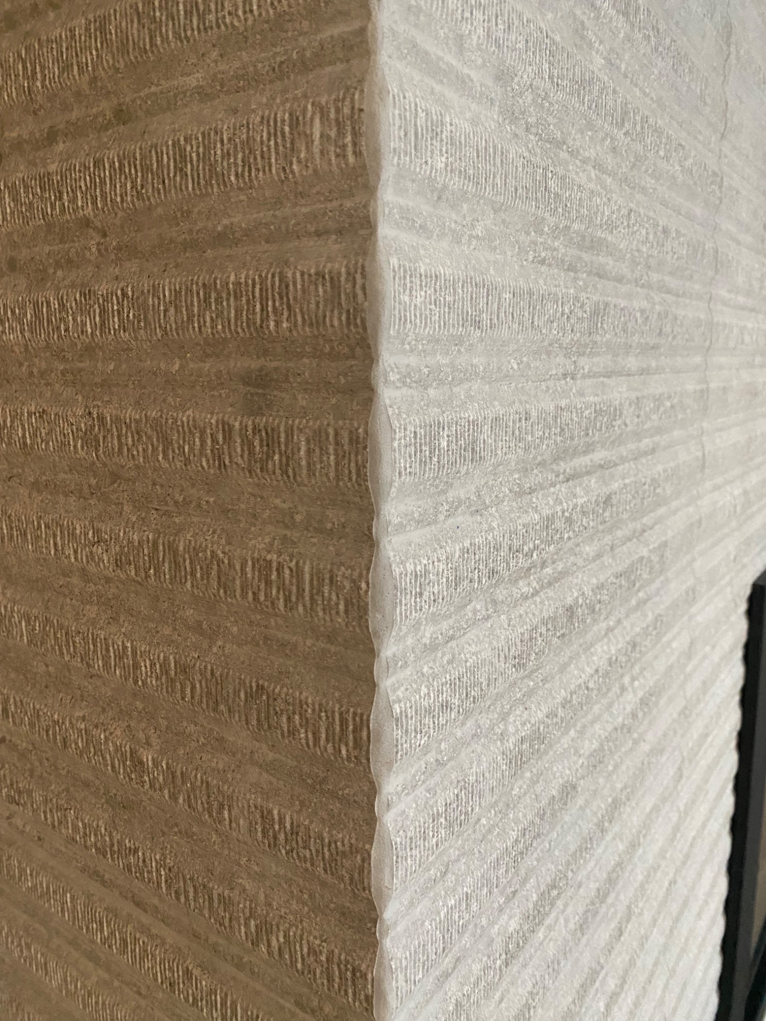 Tekstura ściany z dekoracyjnymi, poziomymi żłobieniami, widoczny narożnik i fragment czarnej ramy.