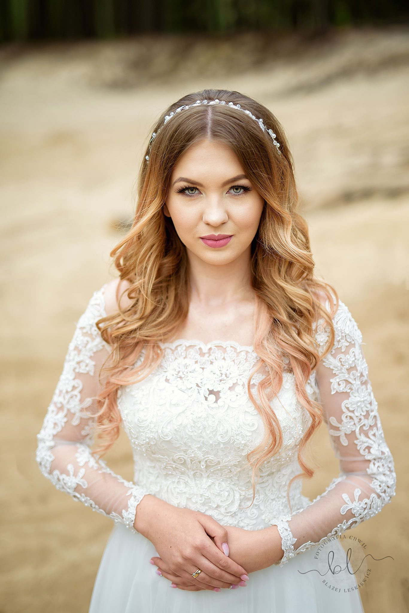 Portret kobiety w białej, koronkowej sukni ślubnej z delikatną ozdobą we włosach, na neutralnym tle.