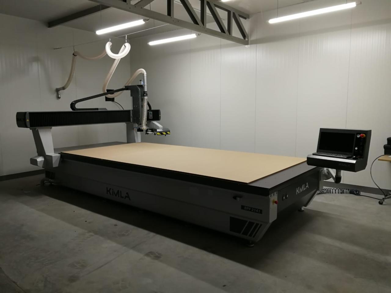 Duża frezarka CNC marki KMLA z panelem sterującym i blatem roboczym z płyty w hali produkcyjnej z oświetleniem jarzeniowym.