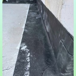 Roof professional Łukasz Bartkowski - Szczegółowe ujęcie izolacji przeciwwodnej z papy na fundamencie budynku, widoczne łączenia i resztki materiału izolacyjnego.