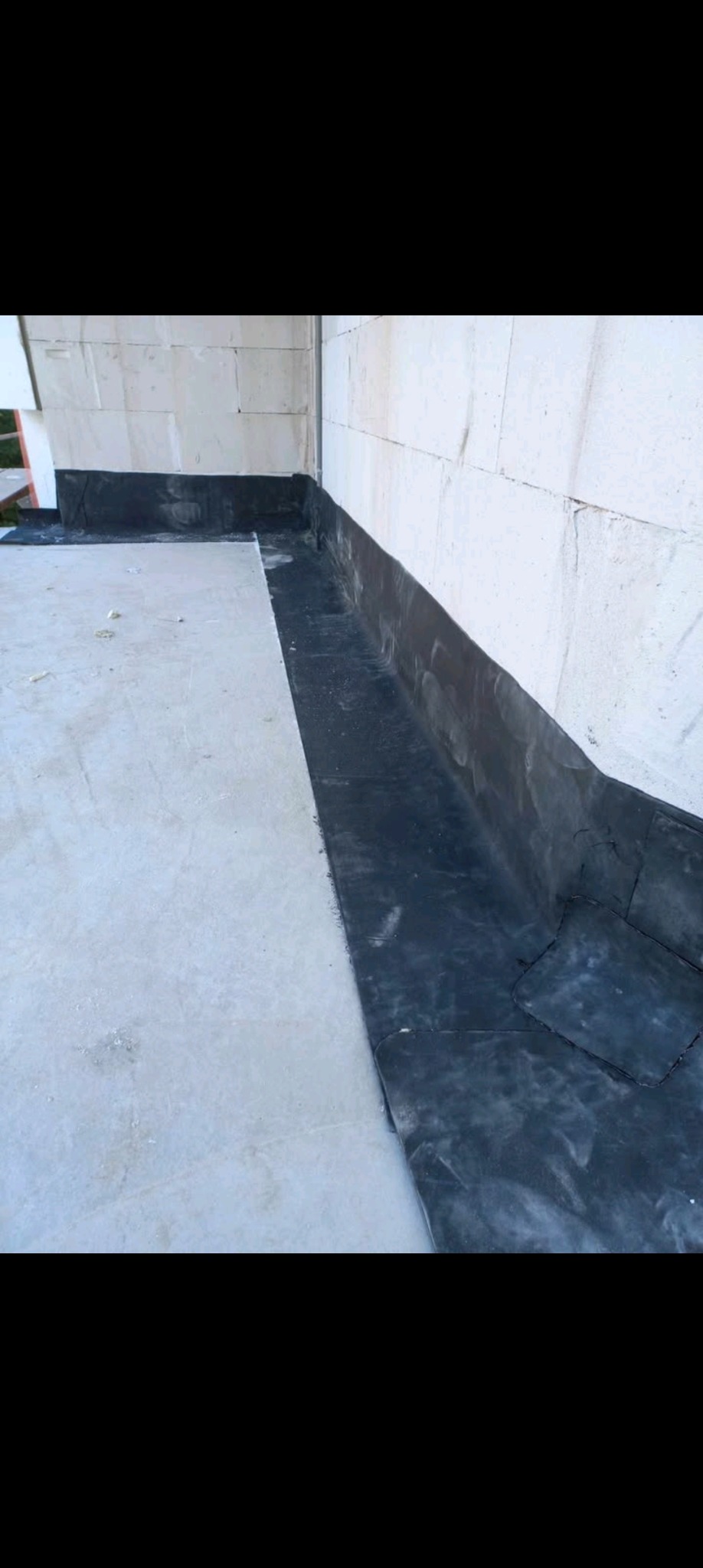 Hydroizolacja w narożniku dachu płaskiego wykonana z czarnej papy bitumicznej, widoczna ściana z bloczków betonowych.