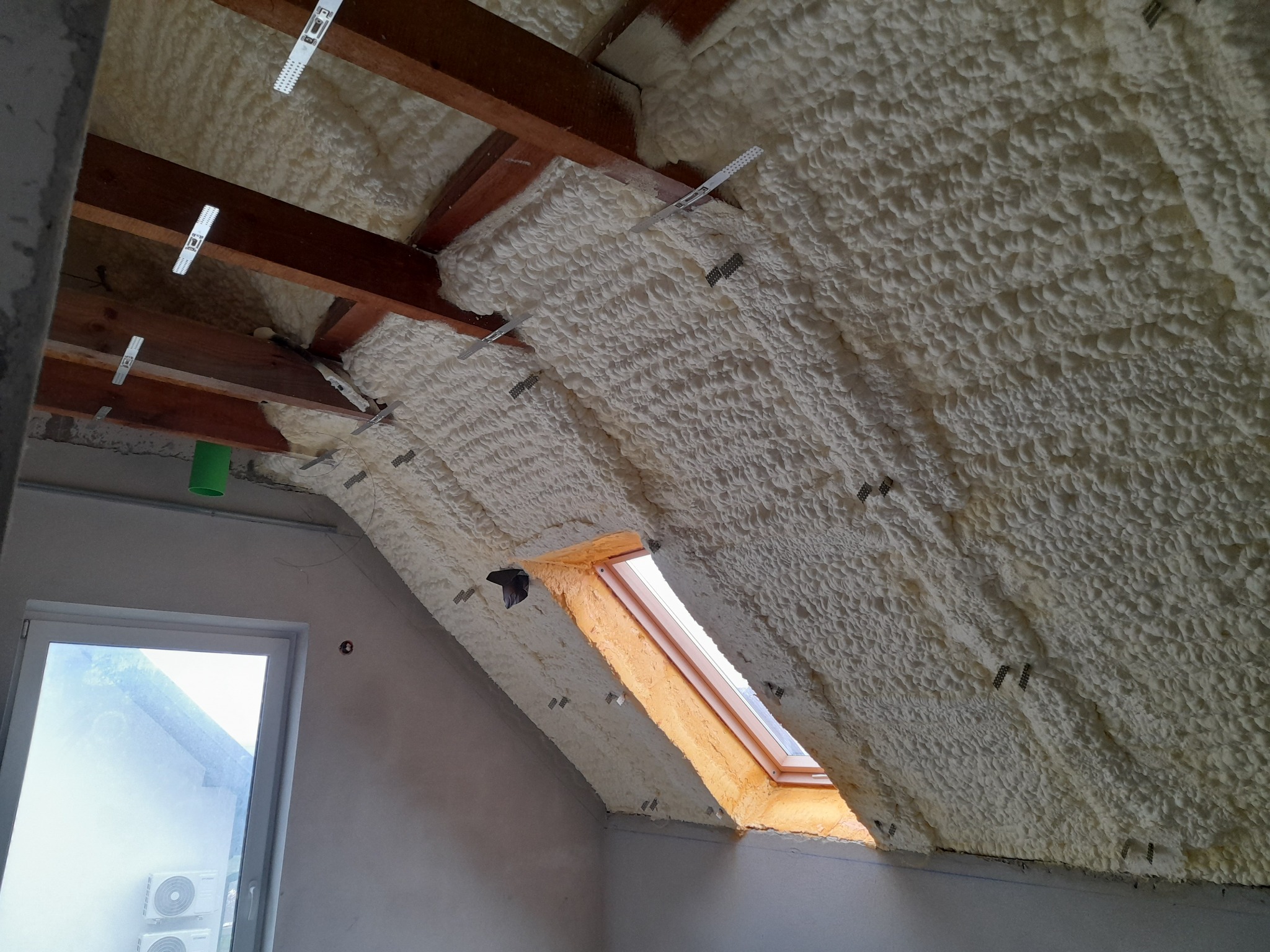 Poddasze ocieplone pianą PUR, widoczne drewniane elementy konstrukcji dachu i okno dachowe.