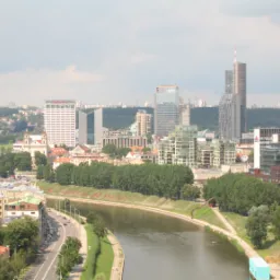 Panorama miasta z rzeką, widoczne nowoczesne budynki biurowe i mieszkalne, zielone tereny rekreacyjne, ruch uliczny wzdłuż nabrzeża.