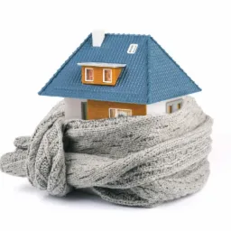 Model domu z niebieskim dachem owinięty szarym, wełnianym szalikiem, symbolizujący izolację termiczną.