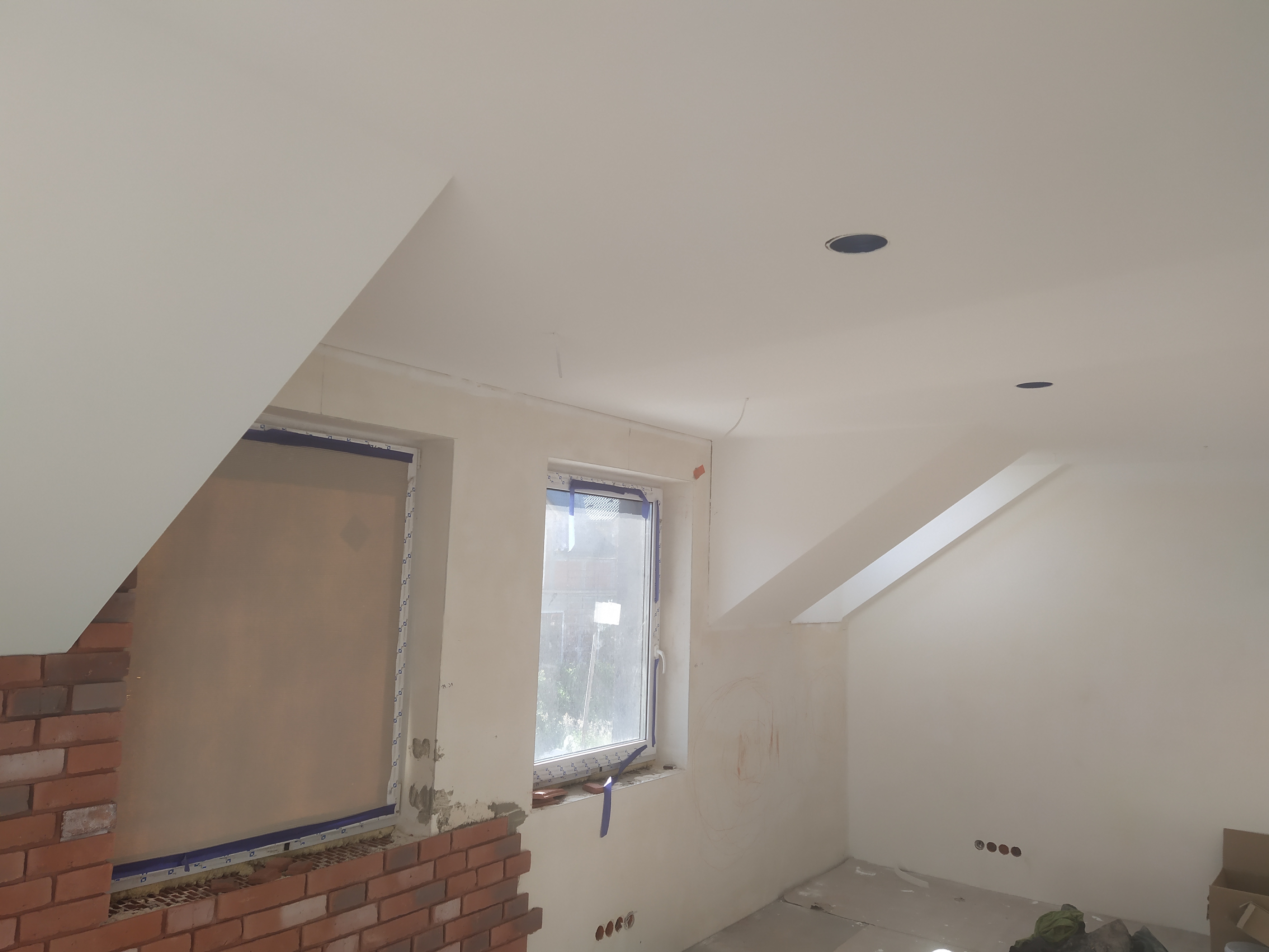 Poddasze w trakcie wykańczania: częściowo położona cegła dekoracyjna wokół okna, przygotowane otwory na oświetlenie w skośnym suficie, okna zabezpieczone folią malarską.